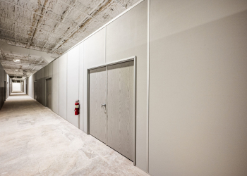 Warehouse interior featuring modular partition walls with a double door and a fire extinguisher mounted on the wall, showcasing a clean and organized layout.