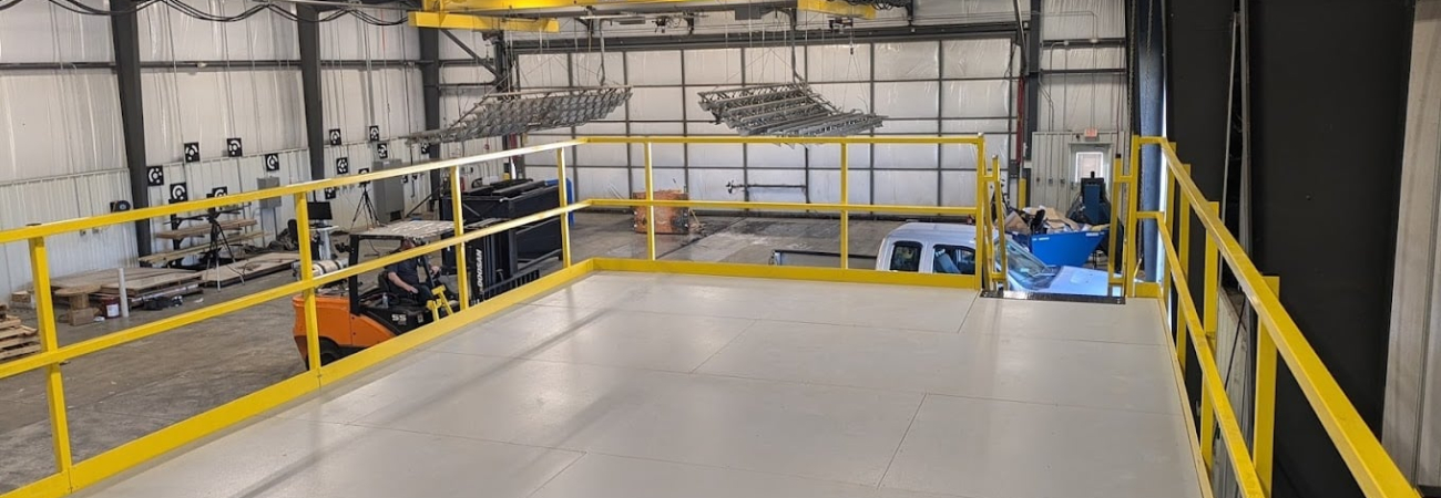Allied Modular pallet racking mezzanine platform installed in a warehouse with yellow guardrails and overhead equipment.