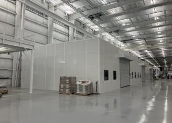 Modular warehouse enclosure with roll-up door and windows built by Allied Modular inside a large industrial facility.