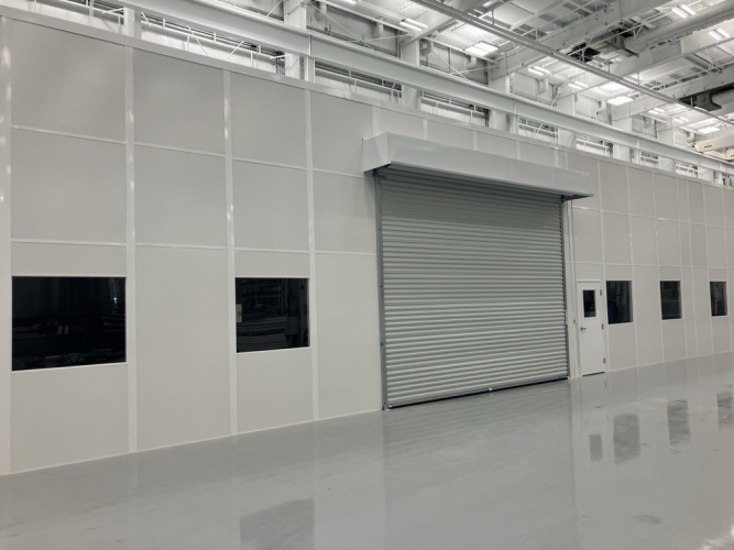 Large modular enclosure with roll-up door and windows, built by Allied Modular inside an industrial facility.