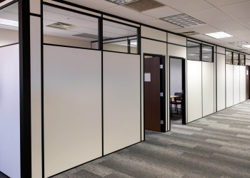 Office hallway with modular partition walls and private offices built by Allied Modular using black-framed white panels and upper glass inserts.