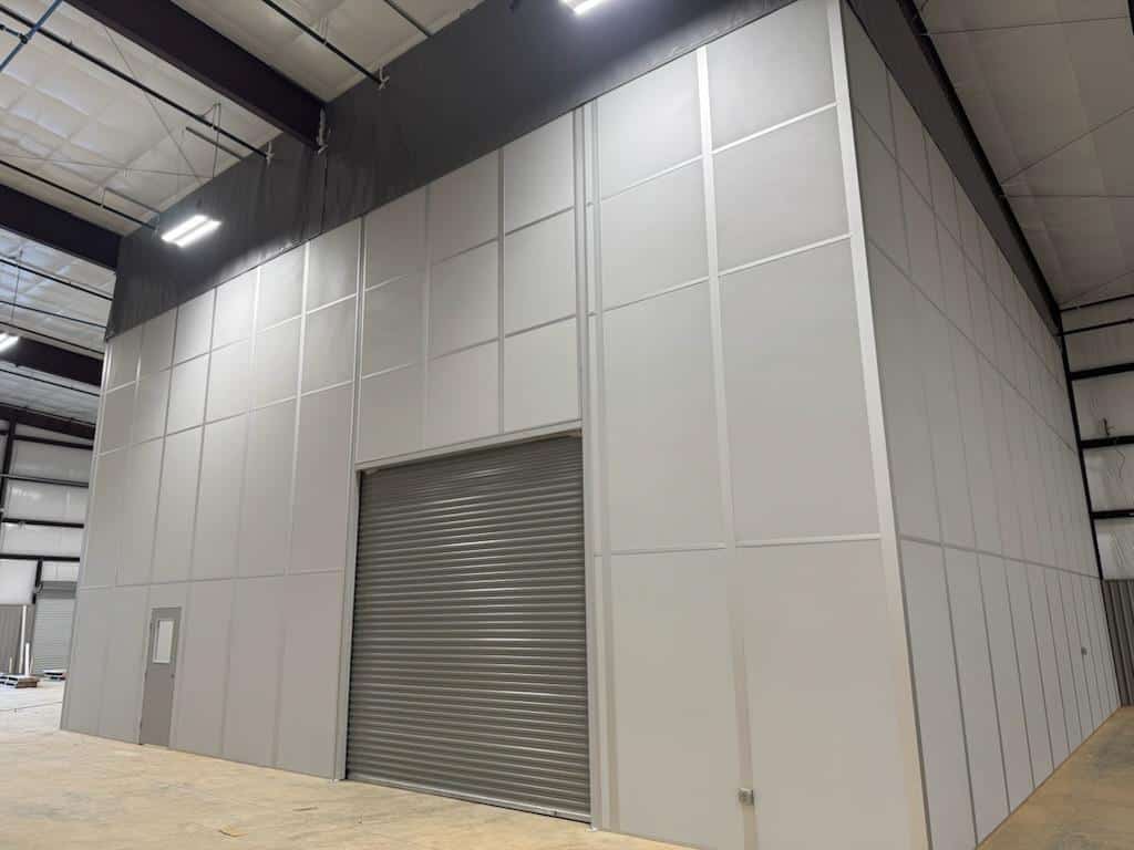 Large modular industrial partition wall enclosure with roll-up door by Allied Modular.