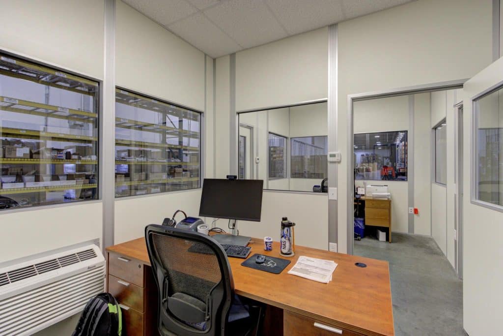 Indoor modular office by Allied Modular with desk, chair, and computer setup inside a warehouse environment.