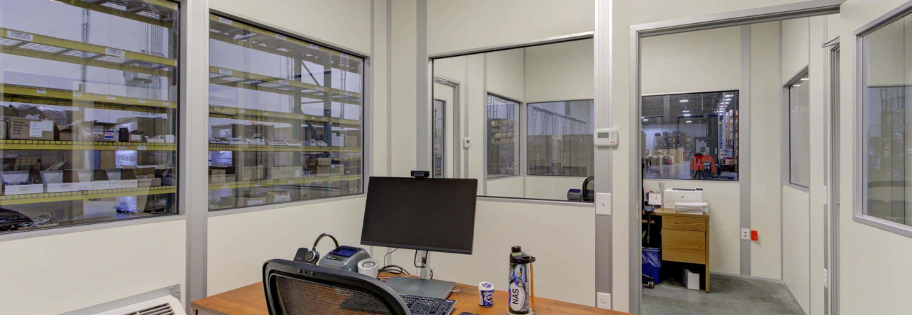 Indoor modular office by Allied Modular with desk, chair, and computer setup inside a warehouse environment.