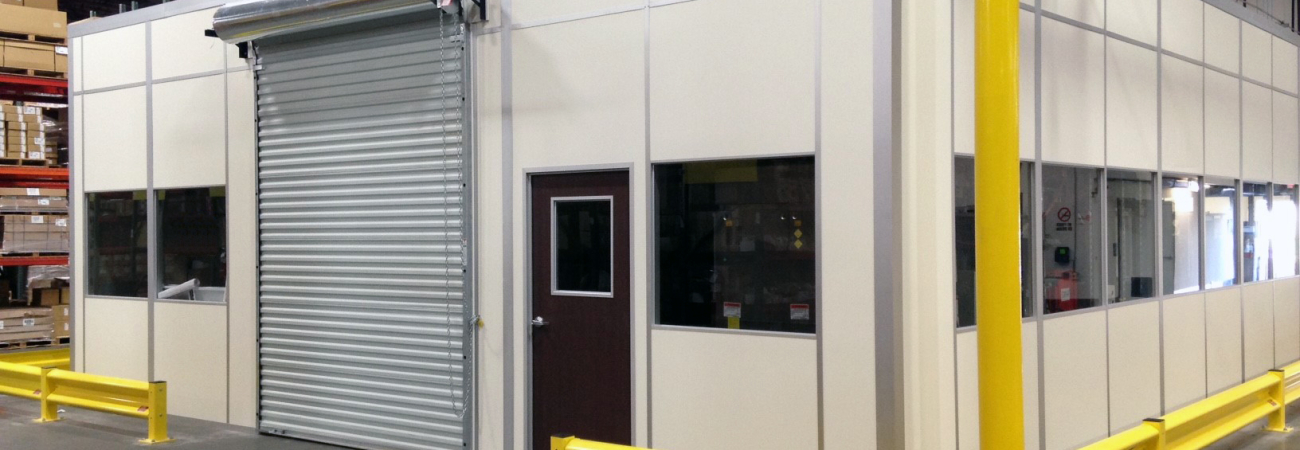 Allied Modular modular office built with prefabricated wall panels, roll-up door, and yellow safety bollards inside a warehouse